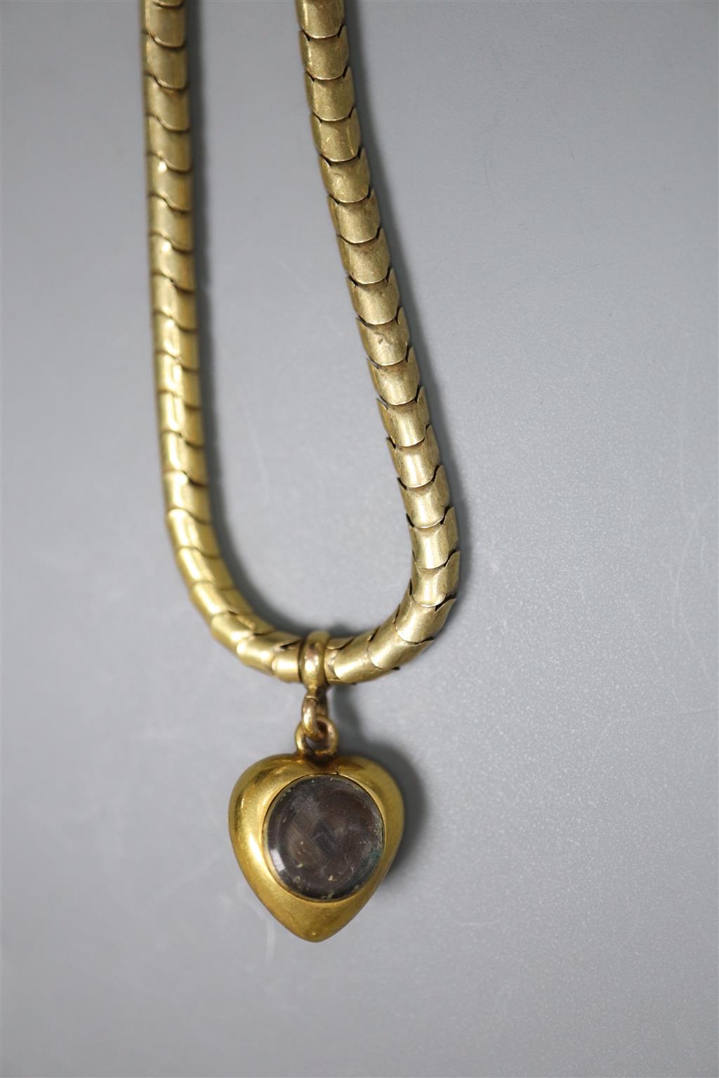A Victorian yellow metal snakelink mourning bracelet, hung with a garnet set heart shaped charm with glazed back,